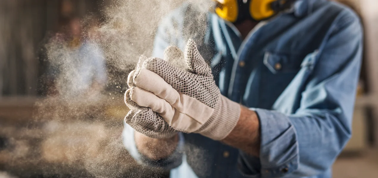 Mann mit Baustellenhandschuhen klatscht in die Hände mit Staub